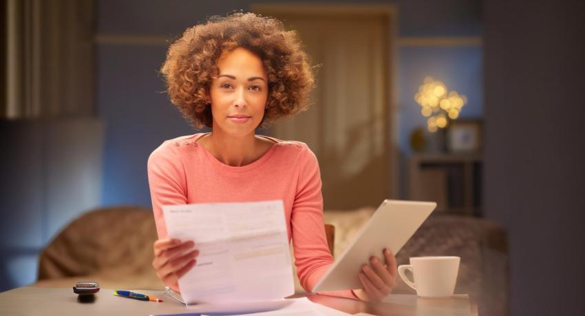 Woman sitting at table, holding ipad and document appearing to be a billing statement