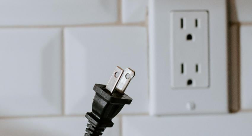 Photograph of an outlet and a hand holding a cable.