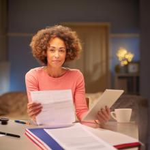 Woman sitting at table, holding ipad and document appearing to be a billing statement
