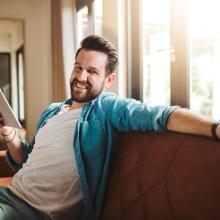 Man smiling, sitting on sofa, holding ipad